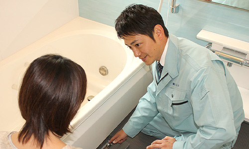 風呂場の様子を見る作業員と女性