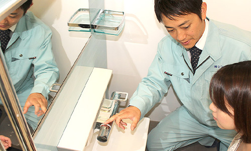 洗面台の様子を見る作業員と女性